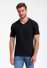 Melnā īsās piedurkņu polo krekls ar ribota raksta virsmu, platu apkakli un pieguļošu siluetu. Apvienots ar gaiši ziliem džinsiem.