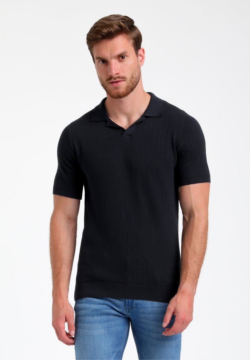 Melnā īsās piedurkņu polo krekls ar ribota raksta virsmu, platu apkakli un pieguļošu siluetu. Apvienots ar gaiši ziliem džinsiem.