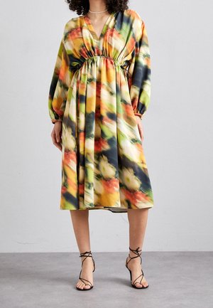 Woman wearing mid-length, long-sleeve dress with multicolor abstract floral pattern and black strappy high-heeled sandals.