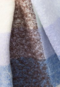 Vilnonis pledas su minkšta tekstūra, pasižymintis šviesiai grietinėlės, rudos ir mėlynos spalvų gradientu; ryškus purus audinys ir abstraktus raštas.