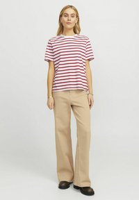 T-shirt riscada em vermelho e branco com gola redonda, combinada com calças largas de cintura alta em bege e botas pretas, contra um fundo simples.