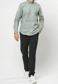 Ljusgrön skjorta med knappar och en liten emblem, kombinerad med mörkgrå byxor och vita sneakers, med en avslappnad passform.