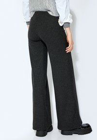 Zijde-brede broek in zwarte stof met witte streepjes. Glad textuur, hoge taille ontwerp, zichtbare achterzak met knoopdetail.