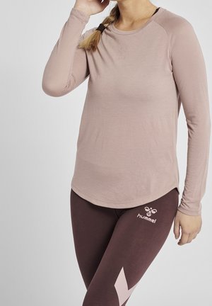 Lange mouwen, lichtroze sporttop met een ronde hals en raglanmouwen. Gecombineerd met donkerbruine leggings met een roze logo en geometrisch ontwerp.
