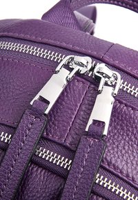 Zaino in pelle viola con superficie testurizzata, dotato di cerniere e tiranti in argento, e accenti di tessuto a contrasto.