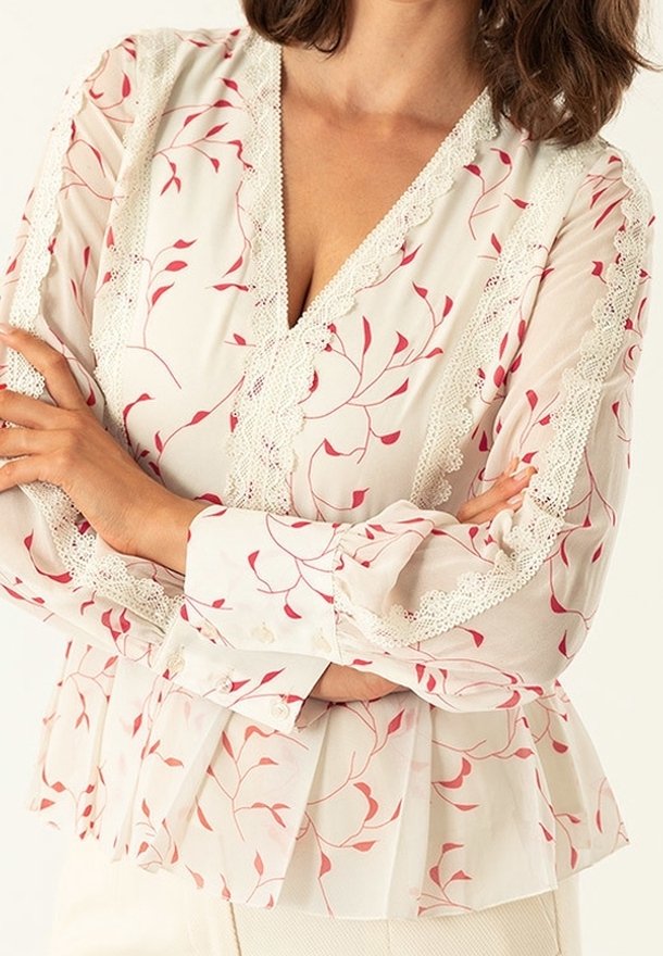 Blusa bianca con motivo floreale rosso, con scollatura a V, bordo in pizzo, maniche lunghe con polsini abbottonati e orlo peplum.