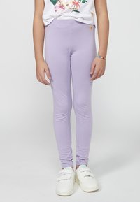 Leggings lilas en tissu extensible, offrant une coupe ajustée. Accentué d'un petit logo doré près de la taille.