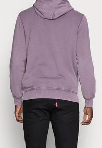 Lila huvtröja med ribbad nederkant och ärmslut. Mjuk tyg med en slät yta, med en logotag på bakfickan.