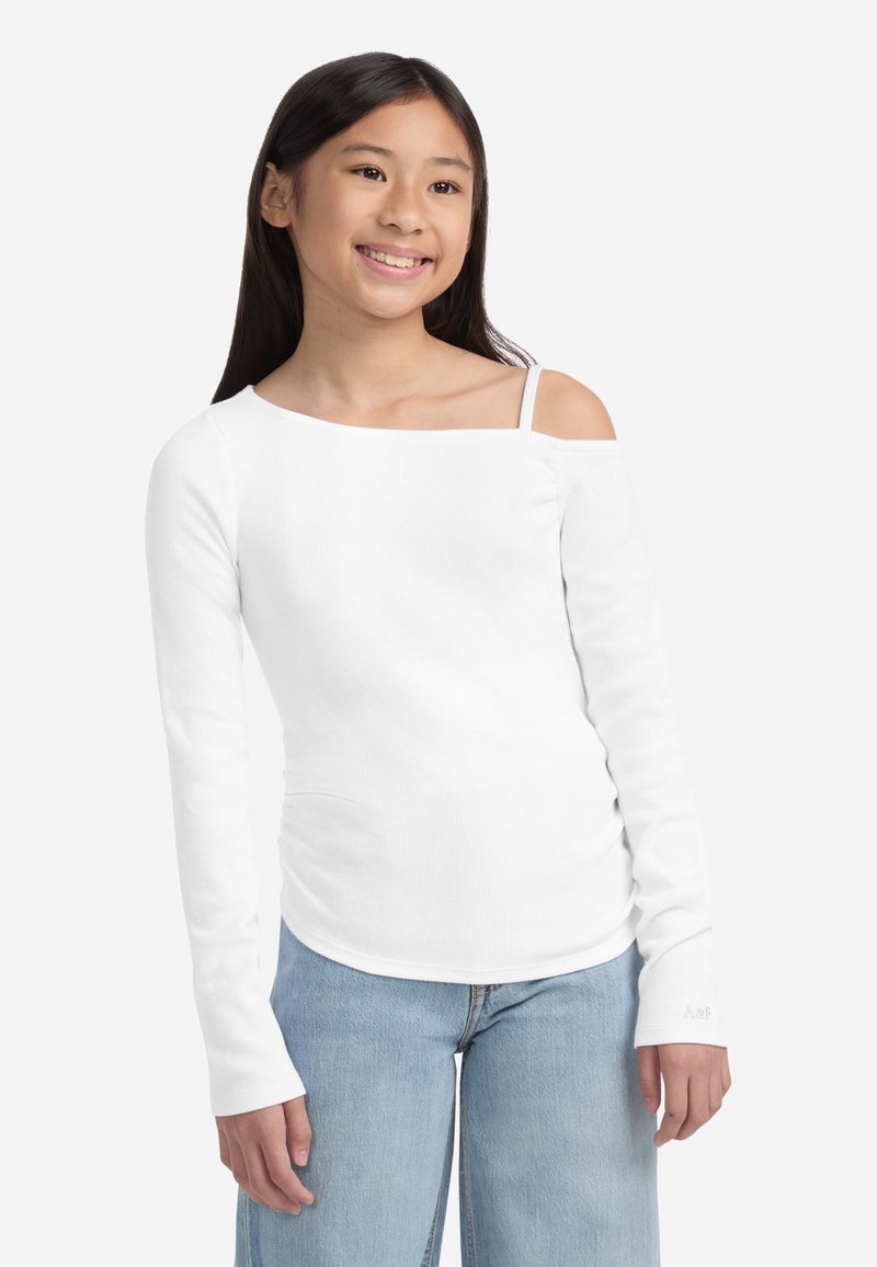 Bela dolga majica s off-shoulder oblikovanjem, rebrasto teksturo in ozkimi naramnicami, v kombinaciji s svetlo modrimi širokimi hlačami.