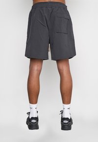 Pantaloni corti grigi con cintura elastica, una tasca posteriore e vestibilità ampia. Abbinati a scarpe da ginnastica nere e calzini bianchi. Texture del tessuto liscia.