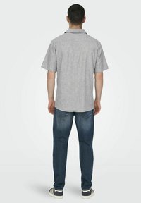 Grå kortärmad skjorta med ett subtilt mönster, parat med mörkblå jeans. Avslappnad passform, rak stil, och vita skor med svarta ränder.