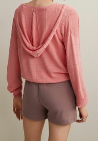 Sudadera corta rosa con un patrón texturizado y capucha, combinada con pantalones cortos gris claro, que presentan un diseño simple y sin hardware visible.