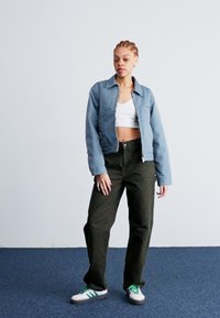 Világoskék cropped dzseki, fehér felső, olajzöld nadrág és zöld kiegészítőkkel ellátott sportcipő. Sima anyag, laza szabás és finom textúrák.
