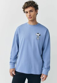 Svetlomodré tričko s dlhým rukávom vyrobené z bavlny, s malou grafikou Snoopy na ľavej strane hrude. Voľný strih s okrúhlym výstrihom.
