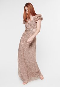 Kimalle hehkiävä rose gold iltal dressi, jossa on röyhelöhihoja, istuva yläosa ja aukko-detailit; virtaava hame, jossa on monimutkaista helmikoristelua ja kimalteleva pinta.