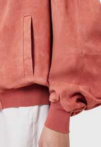 Roze suède jas met een voorvak, geribbelde manchetten en een textuurafwerking. Het ontwerp heeft zachte, ballonvormige mouwen.