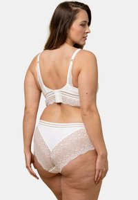Ensemble de lingerie blanc avec des accents en dentelle. Le soutien-gorge a des bretelles réglables et une fermeture à crochets. Le bas taille haute présente un design en dentelle superposée.