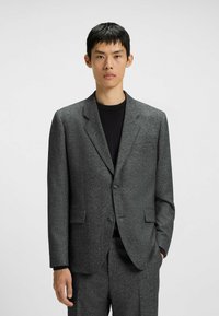 Gray textured blazer with notch lapels, single button closure, and two front pockets, worn over a black top. Tailored fit.