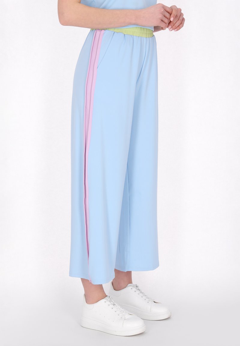 Világoskék, bő szárú nadrág, textúrált, rugalmas derékkal, rózsaszín és zöld oldalsávokkal, fehér sportcipőkkel párosítva.