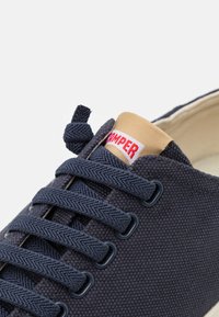 Marineblaue Leinensneaker mit strukturierter Oberfläche, kontrastierendem beigen Zungenbereich, rotem Logotag und klassischem Schnürdesign mit dunklen Ösen.
