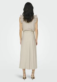 Beige Bluse mit Rüschen an den Ärmelspitzen und Lochmuster, kombiniert mit einem langen, fließenden beigen Rock. Strapsandalen in Beige runden das Outfit ab.