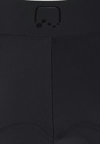 Pantaloni corti sportivi neri con una texture liscia, caratterizzati da un logo lucido in vita e dettagli di cucitura discreti lungo le cuciture.