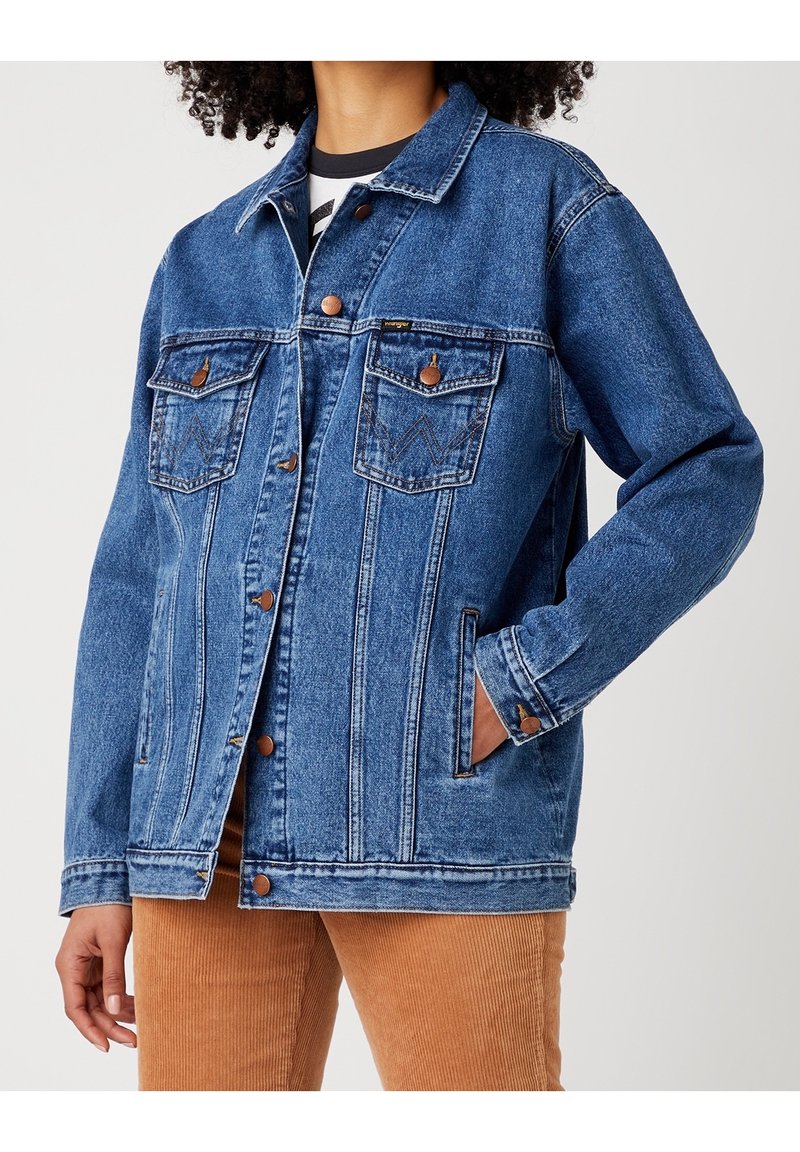 Světle modrá džínová bunda s límečkem, zapínáním na knoflíky, dvěma náprsními kapsami a kontrastním prošíváním. Má dlouhé rukávy a volný střih.