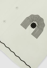 Tissu blanc avec une ligne ondulée noire près du bord, des boutons, et un motif brodé noir de lignes courbes concentriques autour d'une forme d'étoile.