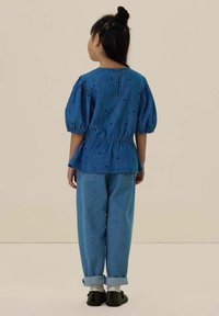 Haut en denim bleu avec des manches bouffantes et une taille froncée, associé à un jean bleu clair retroussé. Le haut comporte de petits pois noirs.