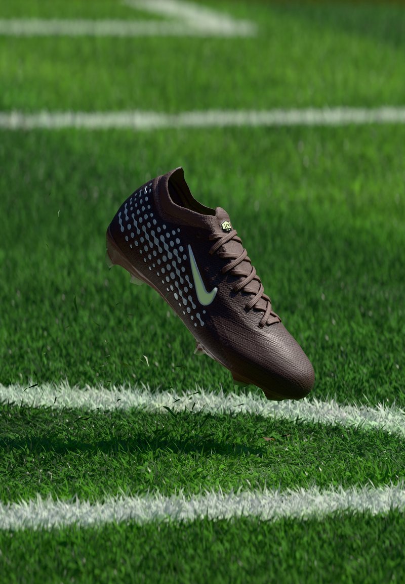 Σκούρο καφέ ποδοσφαιρικό παπούτσι Nike με λευκές κουκκίδες και λογότυπο που αιωρείται πάνω από πράσινο χορτάρι κοντά σε λευκές γραμμές ορίων.
