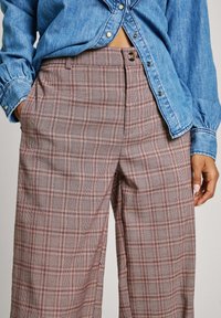 Rutig, vida byxor i rosa, vitt och svart med strukturerad tyg. Har en knäppning fram och sidofickor. Matchat med en denimskjorta.