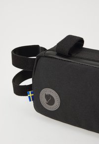 Pochette en tissu noir de forme rectangulaire, dotée d'une sangle Velcro et d'un logo circulaire. Comprend un onglet bleu et jaune.