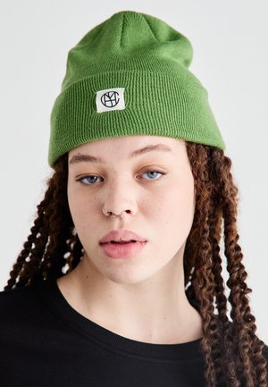 Groene gebreide muts met een geribbelde textuur en een klein geweven label met een zwart logo. De muts heeft een lichte slouch bovenaan.