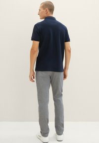 Marineblauwe polo met kraag, gecombineerd met lichtgrijze textuurbroek en witte sneakers, gepresenteerd van achteren.