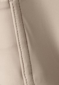 Beige textiel met een geribbelde textuur, met zichtbare stiksels en naden. Het materiaal lijkt glad en licht rekbaar.