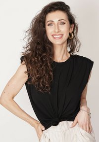 Czarna, luźno dziana koszulka z podwiniętymi rękawami i węzłem w talii, zestawiona z jasnymi spodniami w paski. Miękka tekstura.