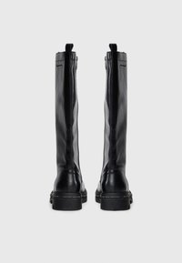 Bottes noires en cuir montantes avec une texture lisse, bout arrondi et semelle épaisse ; elles disposent d'une fermeture éclair sur le côté et d'onglets en tissu.