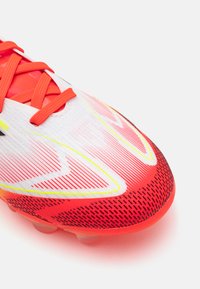 Red and white soccer cleat with textured upper, featuring black and yellow accents, and a streamlined design for optimal performance.