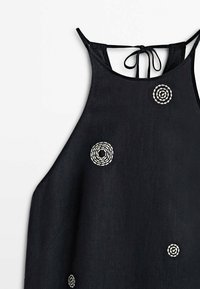 Haut noir sans manches en lin, avec des détails de broderie en spirale blanche. Le modèle possède un lien à nouer au dos et une coupe décontractée.