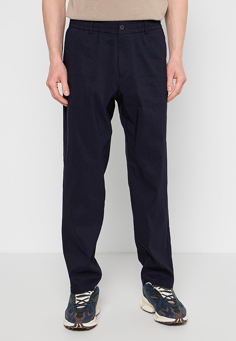 Granatowe spodnie o luźnym kroju, wykonane z lekkiego materiału, z zapięciem na guzik i bocznymi kieszeniami, w połączeniu z teksturowanymi trampkami.
