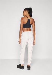 Zwarte sportbeha met dunne bandjes, gecombineerd met lichtroze joggingsbroek met zijstrepen, en zwarte sportchoenen. Gladde stofstructuur.