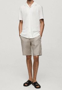 Camisa blanca de manga corta con botones, pantalones cortos beige y sandalias de tipo deslizante negras. Tela ligera, corte relajado y diseño en color liso.