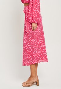 Růžová, midi dlouhá sukně vyrobená z lehkého materiálu s tečkovaným vzorem v různých odstínech. Zavazuje se v pase a jemně splývá.