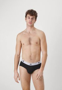 Μαύρα ανδρικά εσώρουχα (briefs) με λευκή ελαστική μέση που φέρει το λογότυπο adidas. Λείο ύφασμα, εφαρμοστή γραμμή και κλασικός σχεδιασμός briefs.