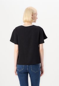 Black short-sleeve top with a textured design and a round neckline. The back shows a relaxed fit and subtle stitching details.