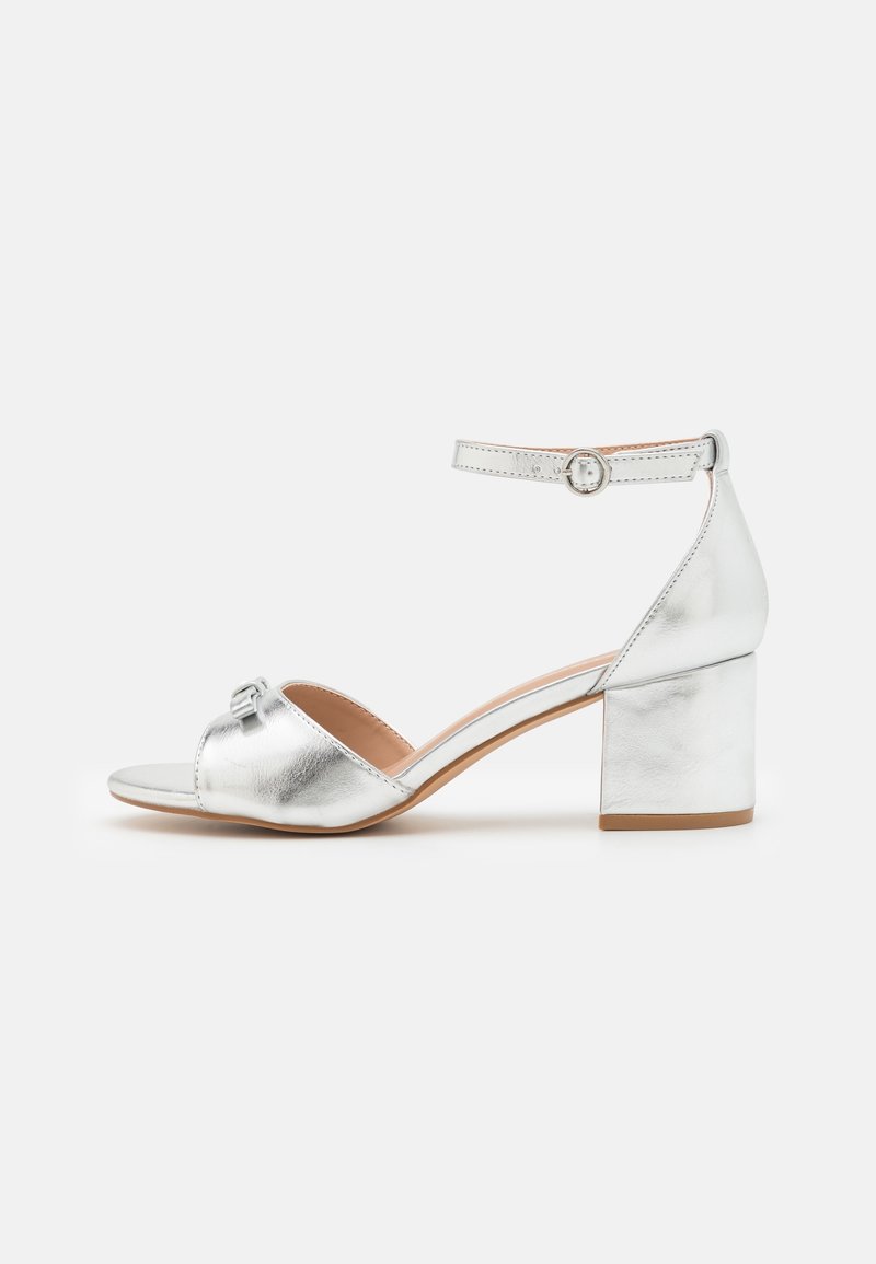 Sandale pour femme argentée à bout ouvert, talon bloc, bride de cheville et fermeture à boucle, montrée de profil sur fond blanc.