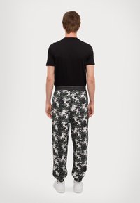 Black short-sleeve shirt paired with gray and black patterned sweatpants; elastic waistband and white sneakers visible.