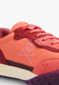 Zapatillas rosas y naranjas con un diseño de calavera y tibias cruzadas, con una parte superior texturizada, acentos contrastantes en burdeos y suela morada.