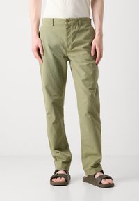 Light green, straight-leg pants made of cotton, featuring a front button closure and side pockets. Paired with brown sandals.