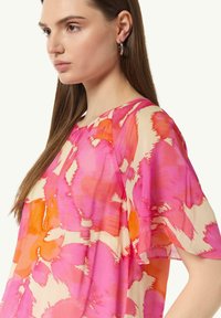 Przejrzysta bluzka z krótkim rękawem w różowo-pomarańczowy abstrakcyjny wzór kwiatowy, z okrągłym dekoltem i zwiewnym materiałem.